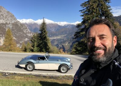 Man standing in front of a classic Austin Healey 3000 on a mountainous road