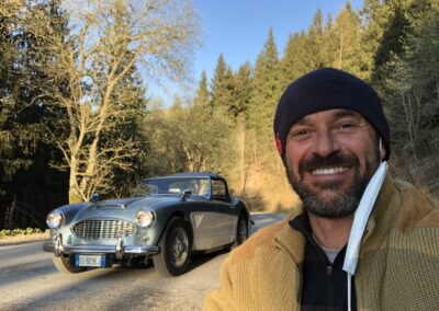 Man standing in front of a classic Austin Healey 3000 in forest in Autumn