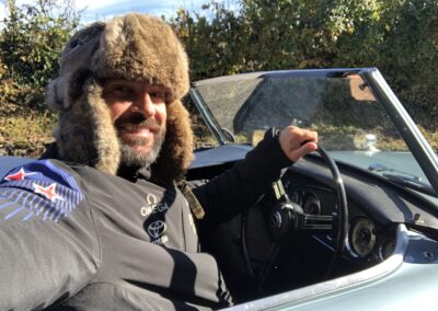 Man smiling from driver seat of a classic Austin Healey 3000 with roof down