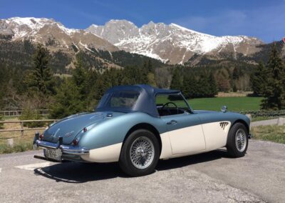 Vintage two-tone Austin Healey 3000 in blue and white parked in front of a mountain