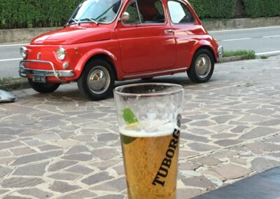 A glass of beer with a vintage red Fiat 500 in the background
