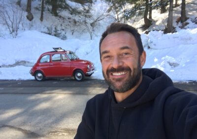 Man smiling in front of a red classic Fiat 500 in the snow
