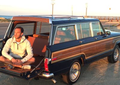 Man sitting on open trunk of a classic Jeep Grand Wagoneer at sunset