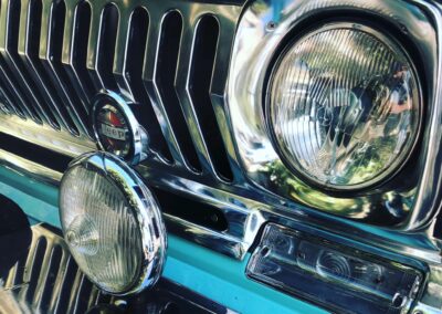 Closeup of front grill and lights of a classic turquoise Jeep