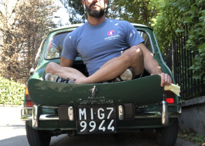 Man sitting cross-legged in the open boot of a green Austin Mini-matic