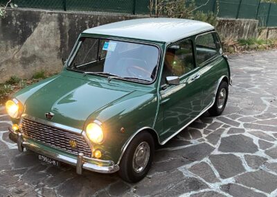 Vintage green Austin Mini-matic parked on street with headlights turned on