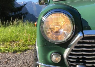 Closeup of a switched on headlight on a green Austin Mini-matic