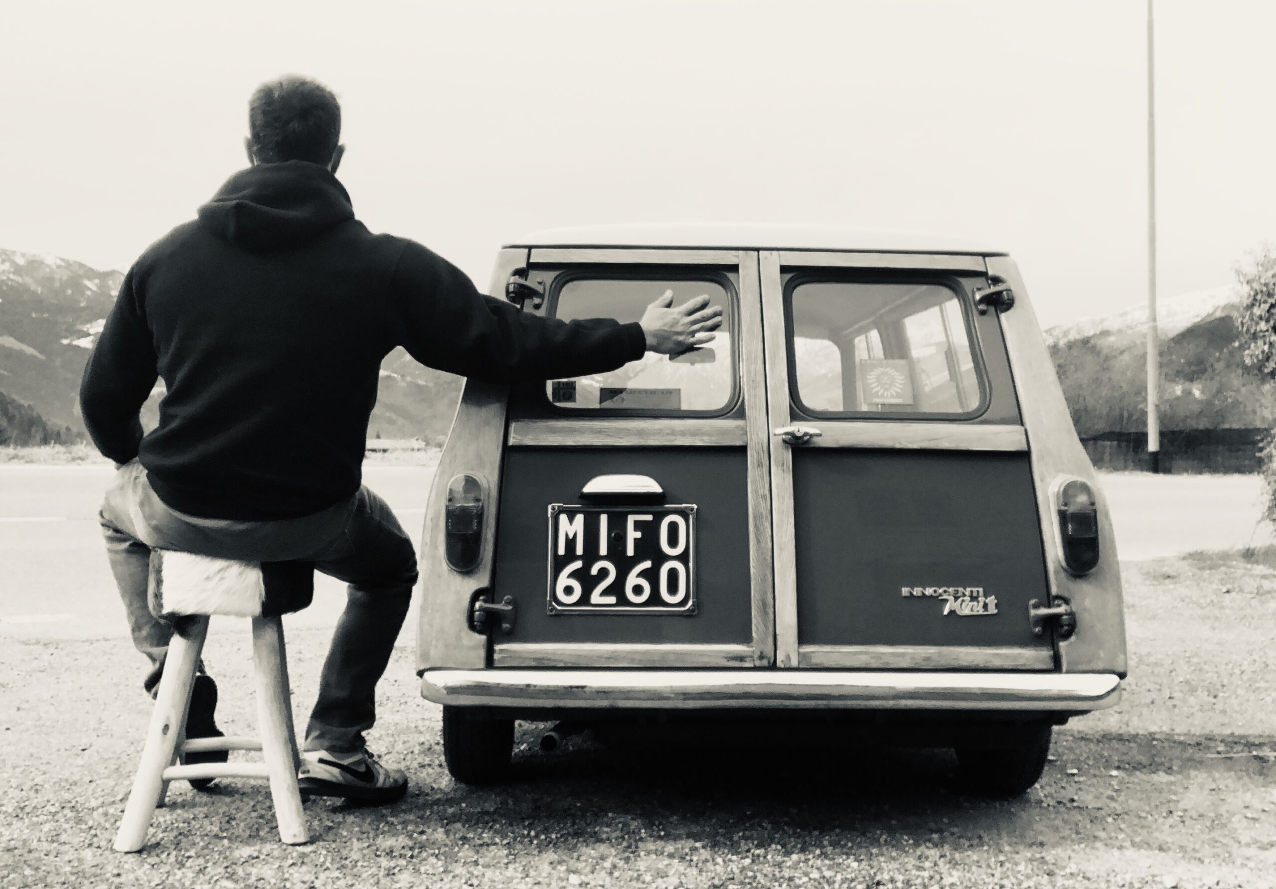 Man sitting beside a Mini Traveller station wagon, seemingly hugging the car