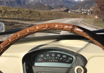 View of steering wheel and dashboard from inside a vintage cream car towards a mountain