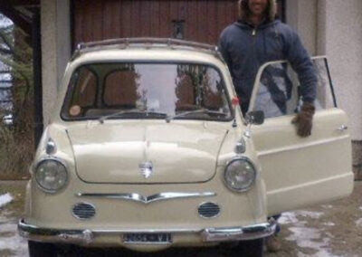 Man in snow clothes standing beside an open beige classic NSU Prinz