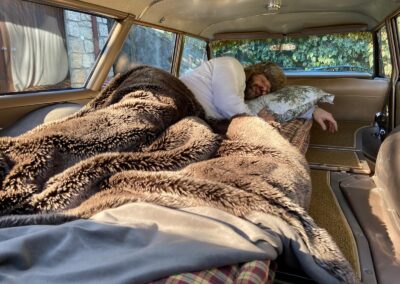 Man sleeping inside Ford Galaxie 500 station wagon under furry blanket