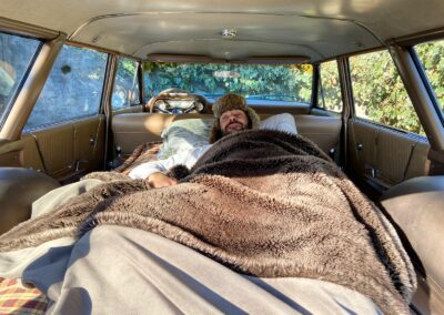 Man waking up on bed inside vintage Ford station wagon