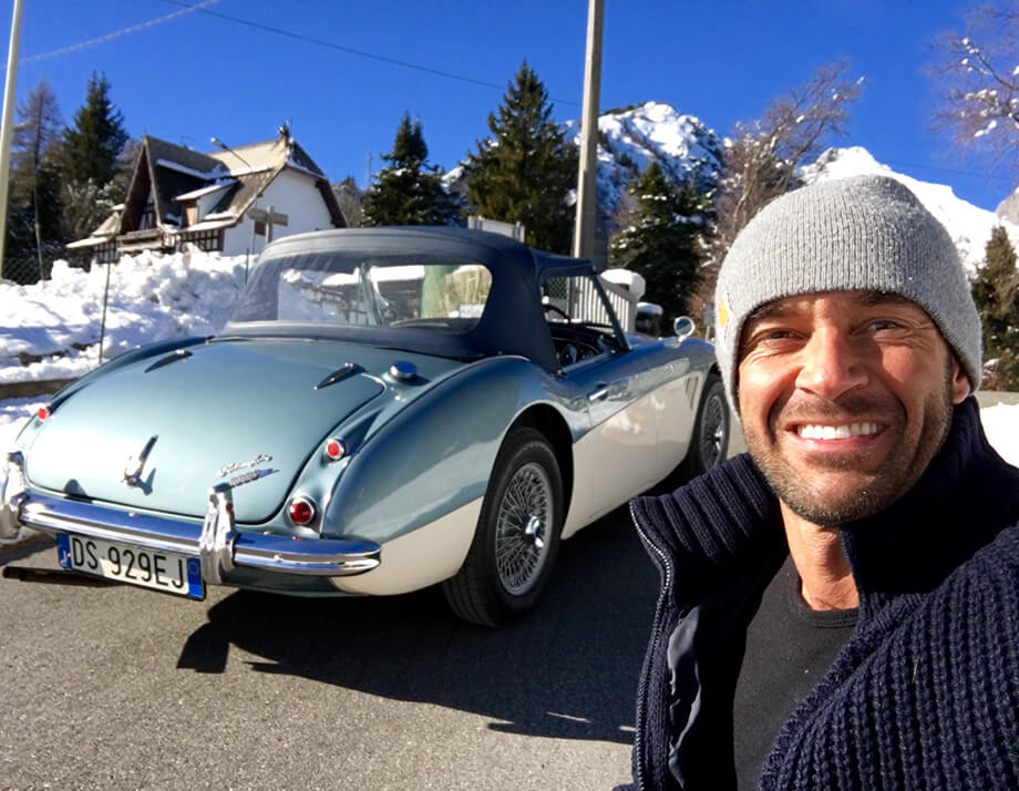 Man smiling in front of an Austin Healey 300 in the snow