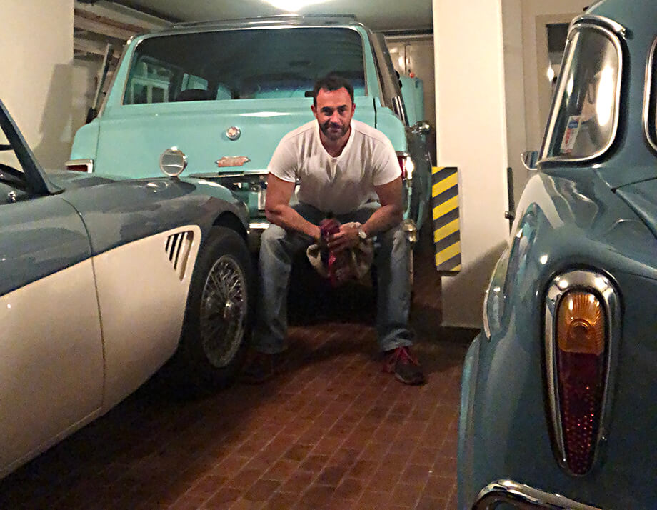 A man working in a classic car garage, surrounded by 3 cars